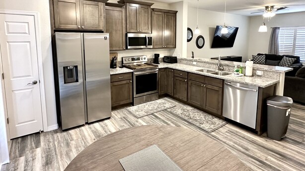 A modern kitchen with stainless steel appliances, wooden cabinets, granite countertops, and a built-in oven. - Newly Built Home Close to River (Bullhead City)