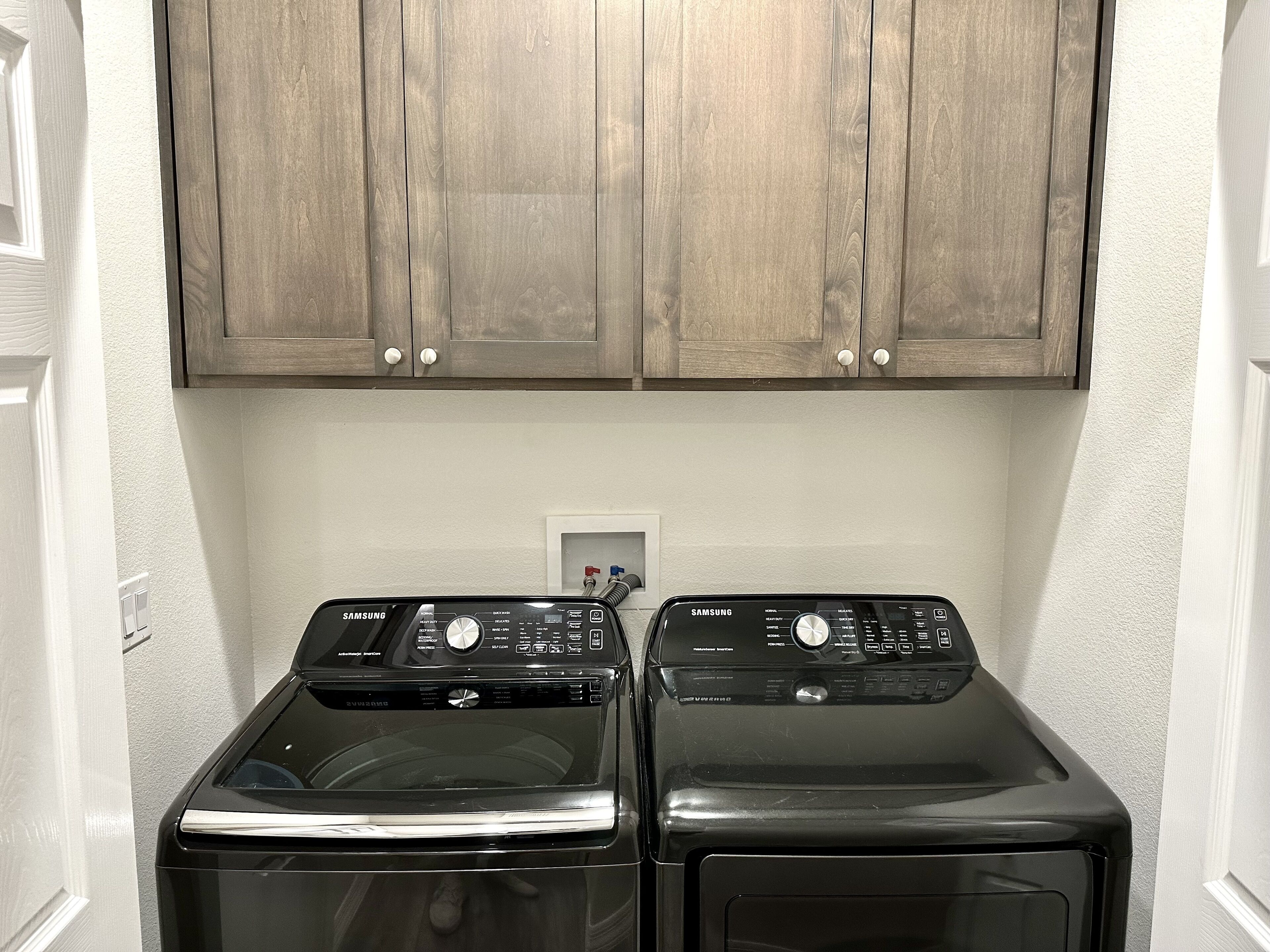 A laundry area with two front-loading washers and a wooden cabinet above.