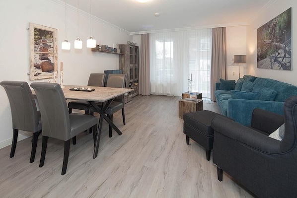 Una sala de estar moderna con comedor, que incluye una mesa de madera, sillas grises, un sofá azul verdoso y un armario.