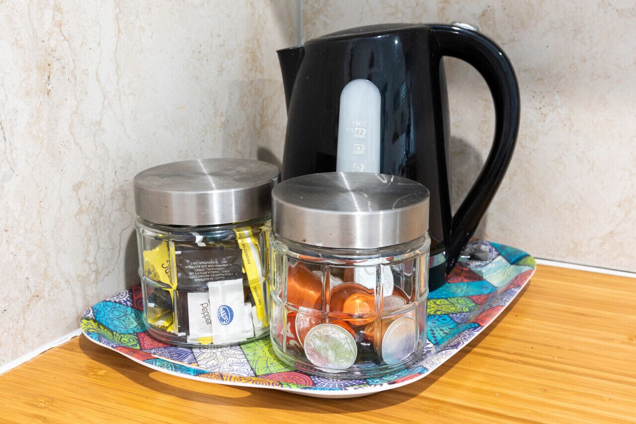 Two glass jars with metal lids on a colorful tray, a black kettle, and a patterned coaster.