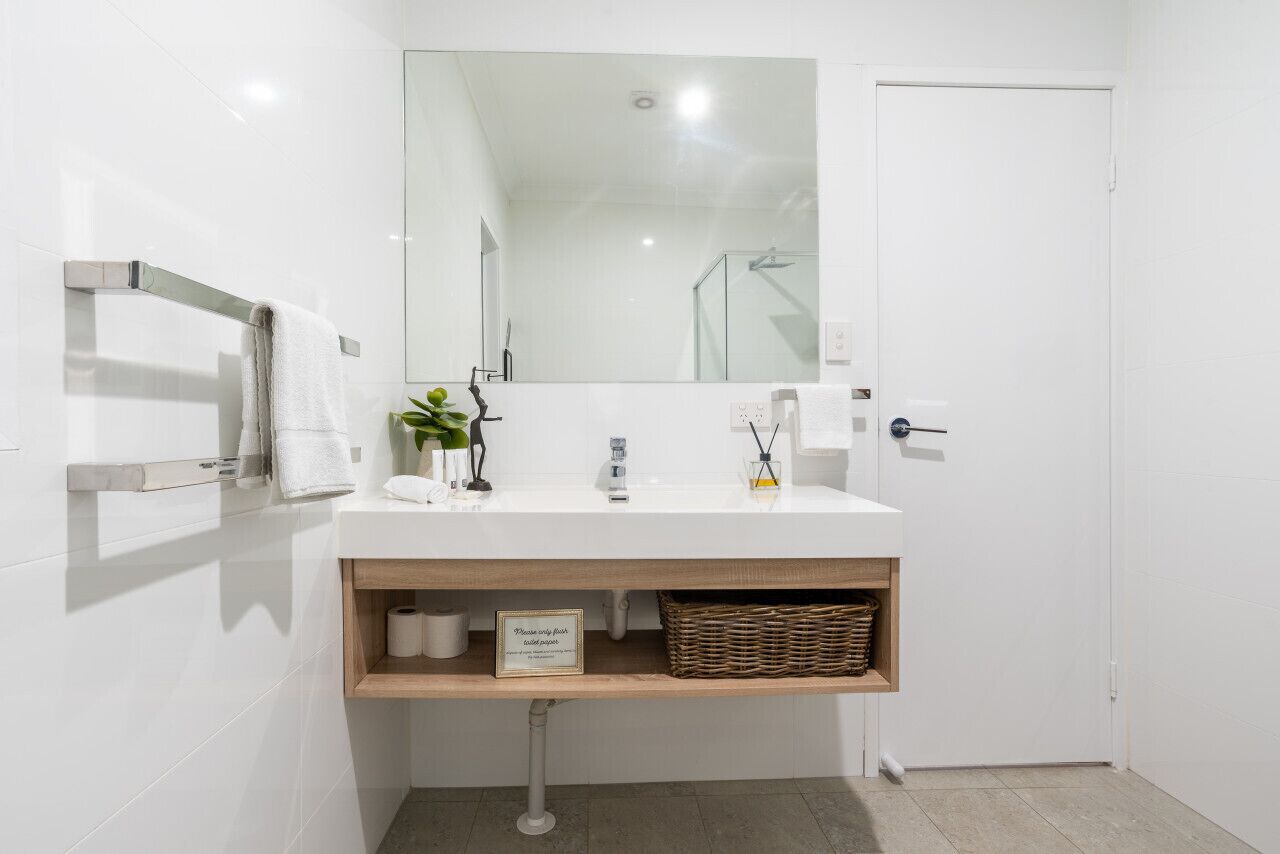 Un baño moderno con un tocador blanco, un espejo, un perchero para toallas y una cesta de mimbre.
