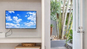 A room with a television on the wall, a wooden cabinet with drawers, and a view of a bamboo garden through an open door. - Contemporary Studio in the heart of Paddington (Paddington)