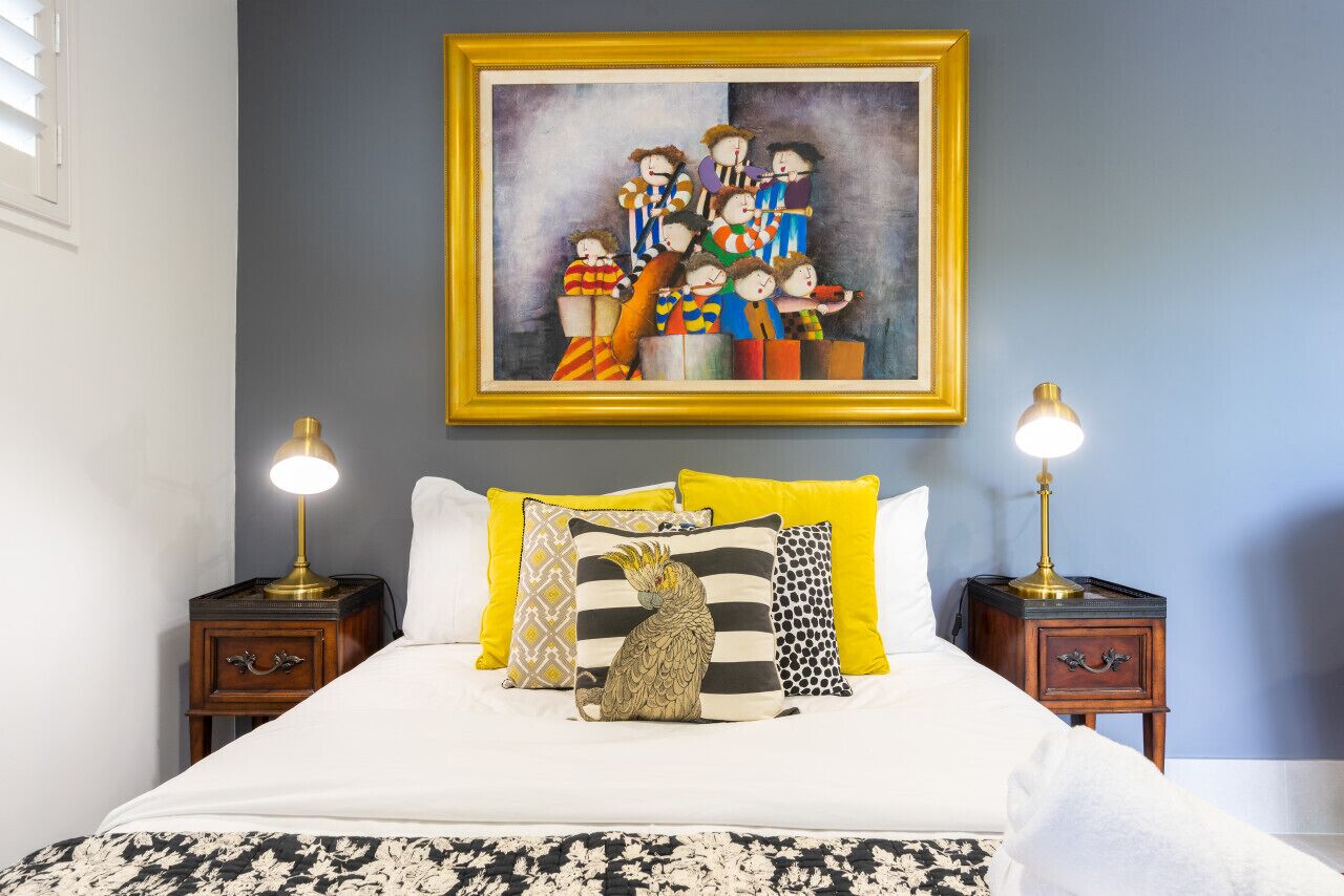 A bedroom with a bed, pillows, a nightstand, a lamp, and a painting on the wall.