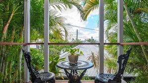 A balcony with two ornate black chairs and a small round table, surrounded by lush tropical plants and a view of a cityscape. - Contemporary Studio in the heart of Paddington (Paddington)
