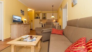 Una sala de estar con sofá, una mesa de centro, televisión y una cocina al fondo.