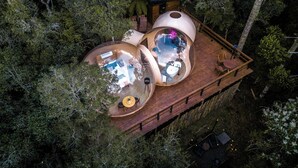 A treehouse with multiple circular rooms, each with a small table and chairs, surrounded by dense forest.