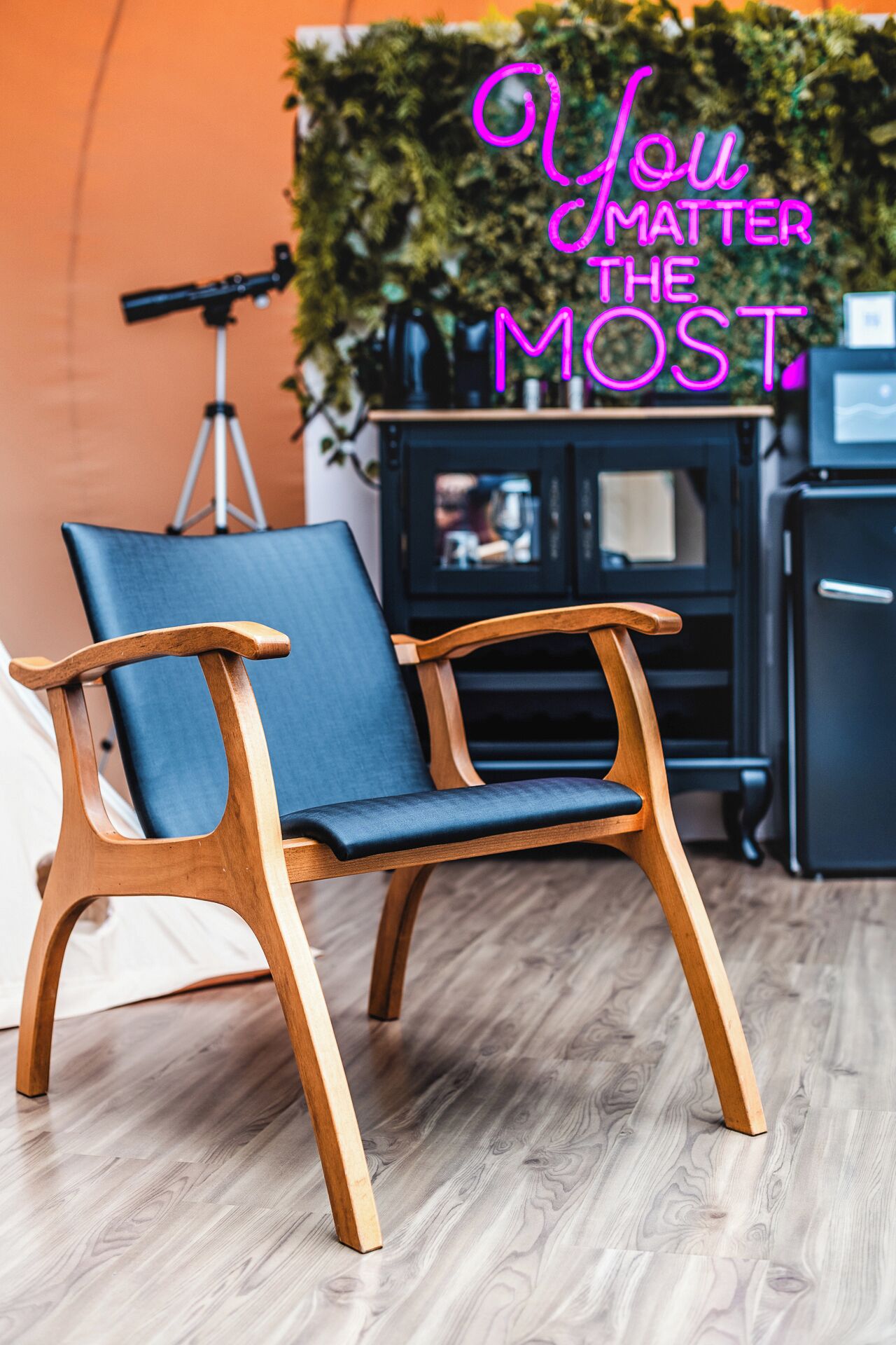 A wooden chair with a blue cushion in a room with a wooden floor and an orange wall.