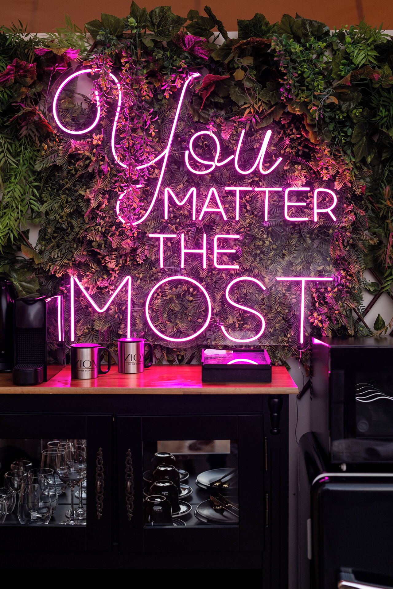 A neon sign with the message "You Matter The Most" against a backdrop of green foliage.