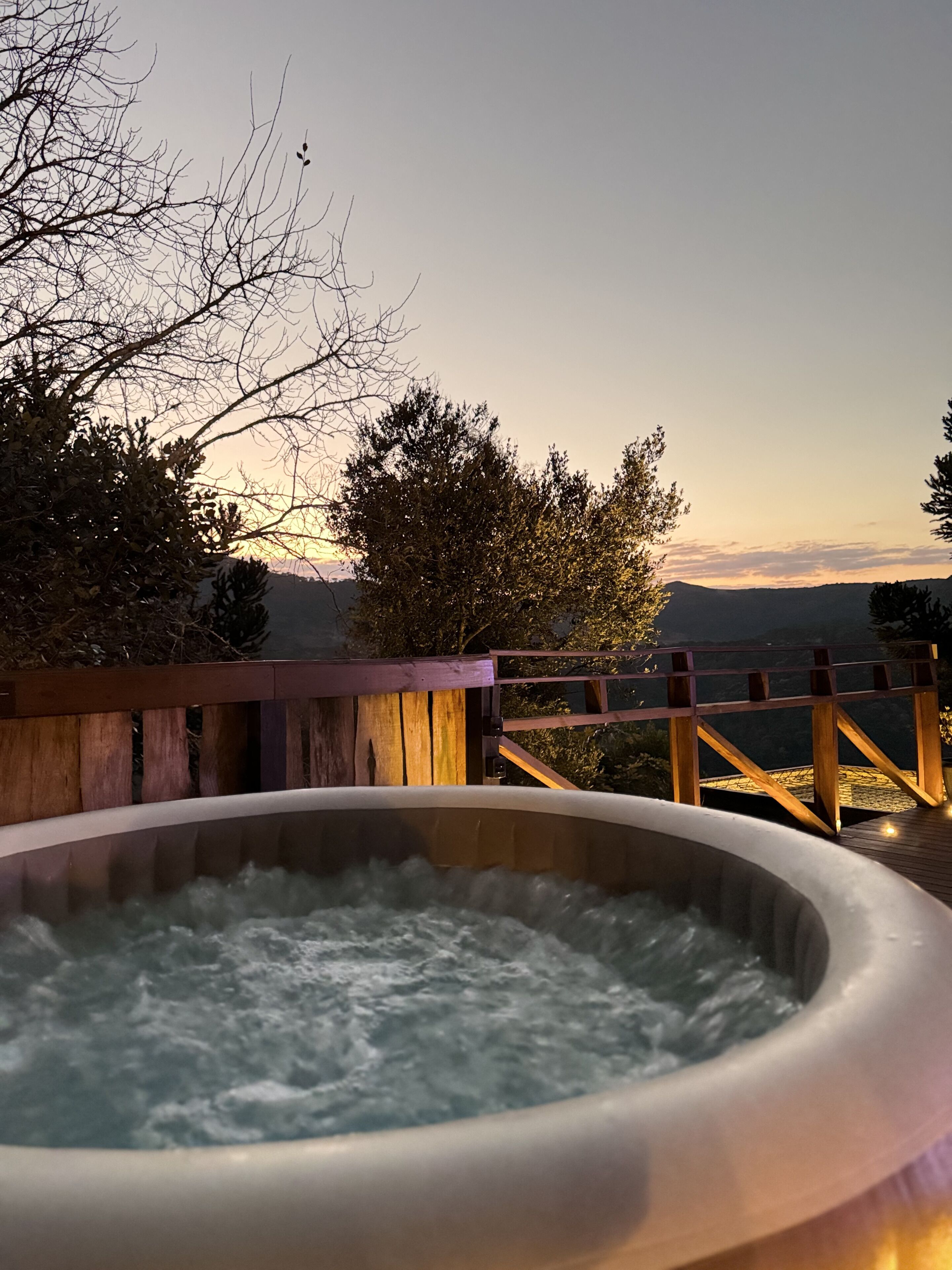 A hot tub on a wooden deck with a view of trees and hills in the background.
