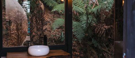 Un bagno con un mobile vanitario in legno, un lavandino bianco e un'ampia finestra con vista su una foresta.