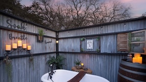 Un baño al aire libre rústico con bañera, velas y un cartel que dice 'Soak Breathe'.