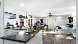 Una cocina moderna con encimera negra, armarios blancos y una zona de comedor con mesa y sillas.