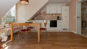 A modern kitchen with white cabinets, a wooden dining table, and red chairs. - Ruhige, Hübsche Ferienwohnung in Strandnähe mit Balkon am Idyllischen Stadtwald (Ostseebad Kühlungsborn)