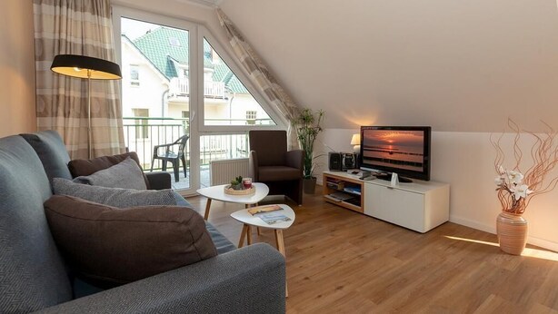 A modern living room with a sofa, TV, and a small table. - Ruhige, Hübsche Ferienwohnung in Strandnähe mit Balkon am Idyllischen Stadtwald (Ostseebad Kühlungsborn)