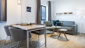 Un salon moderne avec un canapé gris, une petite table ronde et un coin repas comprenant une table et des chaises en bois.