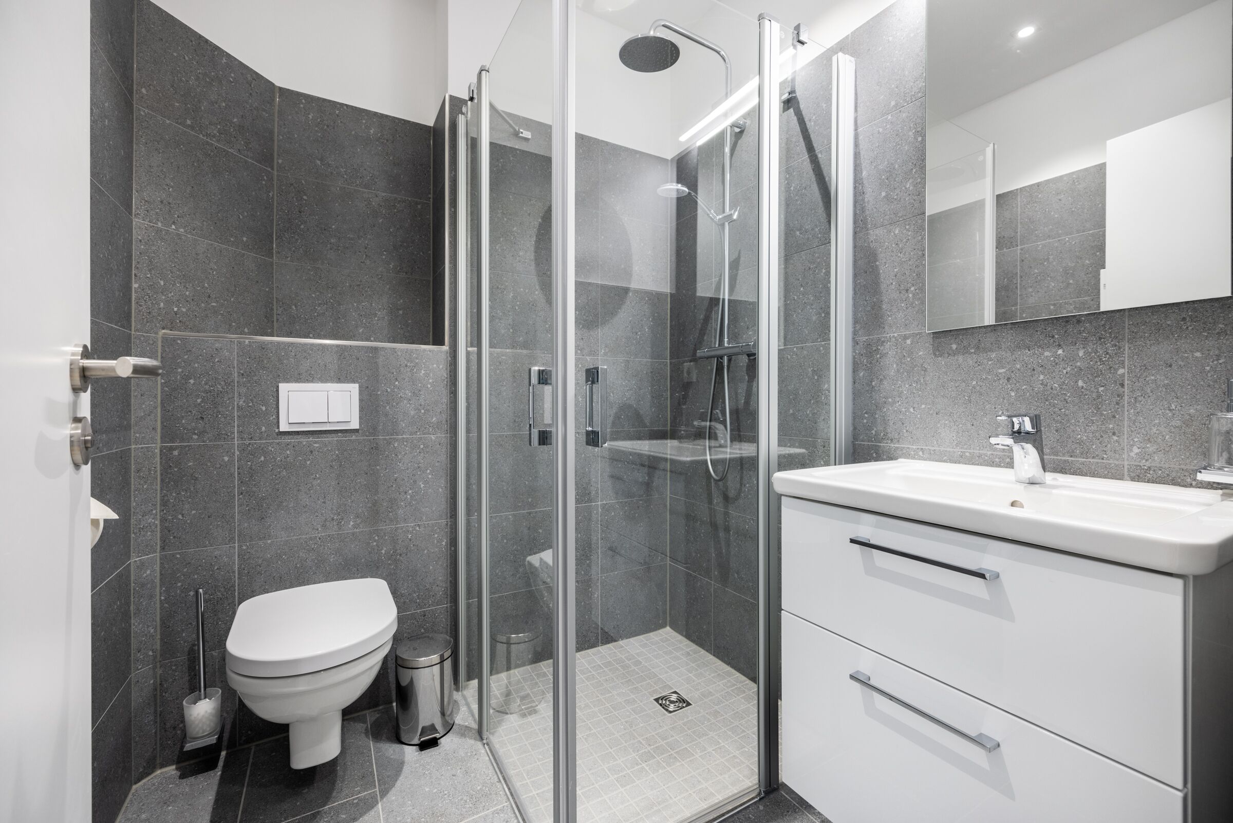Een moderne badkamer met een douche met glazen wand, een wit toilet en een wastafelmeubel met wastafel.