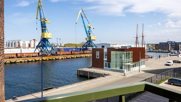 Une vue sur le front de mer, avec deux grandes grues, un bâtiment moderne doté de grandes fenêtres et une zone de quai.
