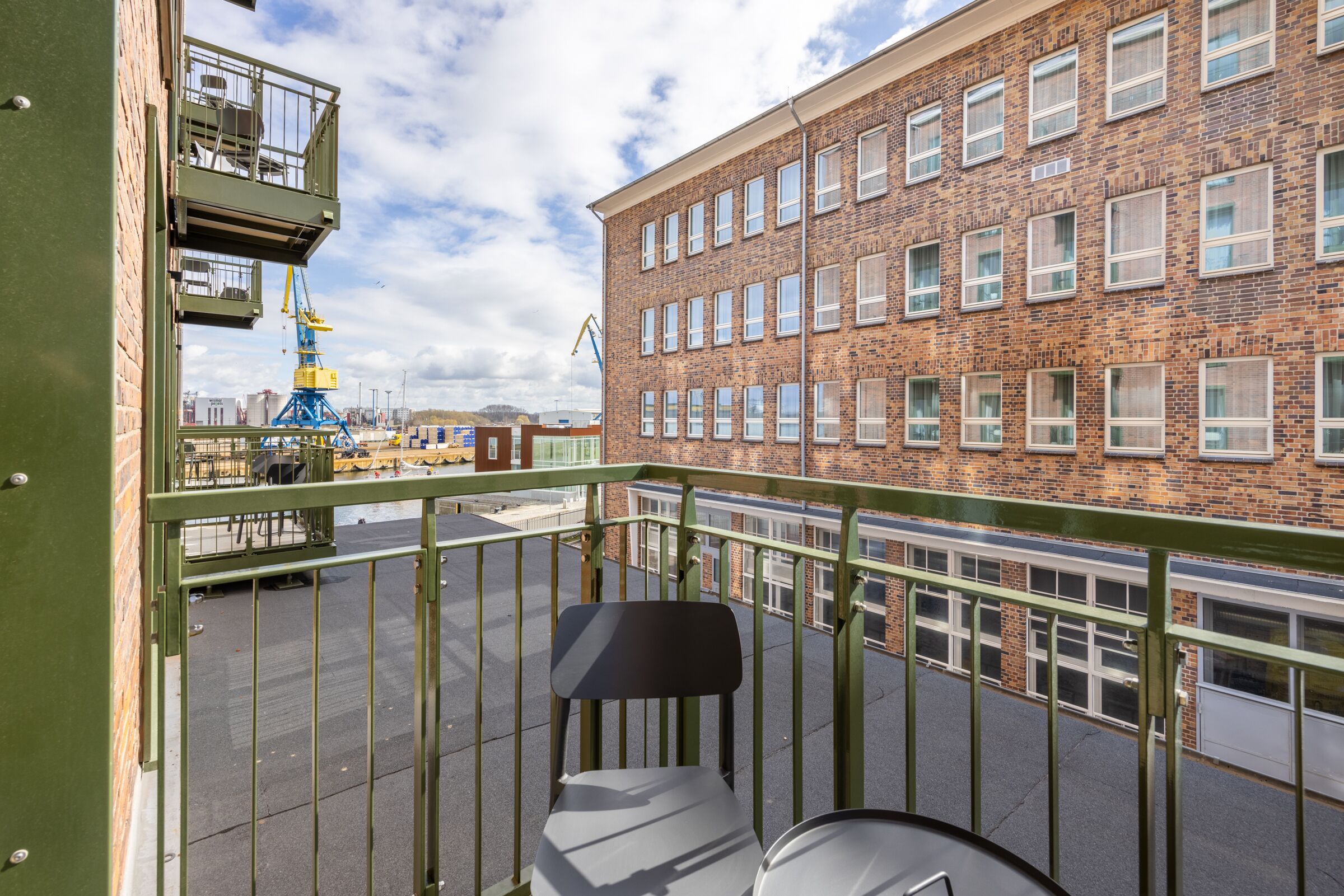 Een balkon met een metalen hekwerk dat uitkijkt over een gebouw van baksteen met meerdere ramen.