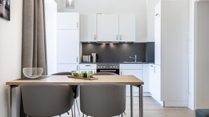 Una cocina moderna con armarios blancos, una mesa de madera, dos sillas grises y una encimera negra.