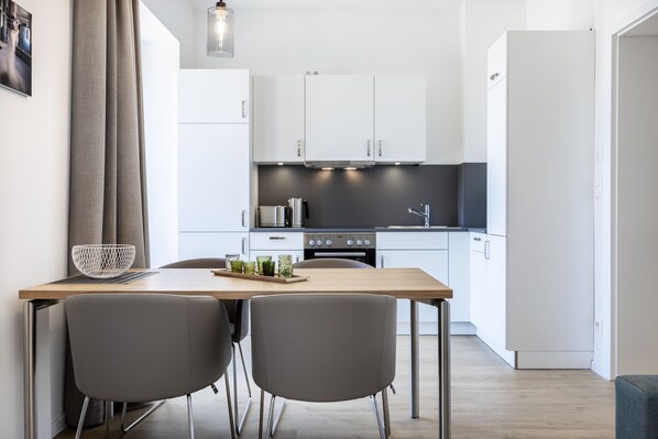 A modern kitchen with white cabinets, a wooden table, two grey chairs, and a black countertop.