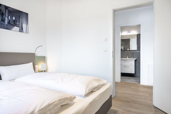 Un dormitorio moderno con cama, lámpara de noche y vista al baño.