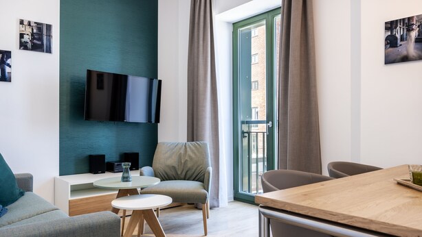 Un moderno salón con televisor de pantalla plana, un sofá, una mesa de comedor y vistas al exterior a través de un ventanal.