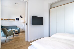 Ett modernt hotellrum med en säng, en soffa, en stol, ett litet bord, en tv som är monterad på väggen och en garderob.