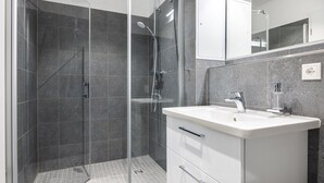 Ein modernes Badezimmer mit einer gläsernen Duschkabine, einem weißen Waschbecken und einem Spiegel darüber.