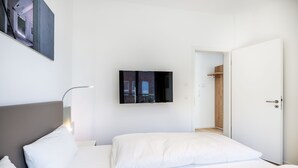 Una habitación de hotel moderna con una cama grande, un televisor de pantalla plana montado en la pared y un armario de madera.