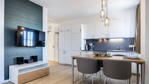 Una cocina moderna con un televisor de pantalla plana, armarios blancos y una mesa de comedor de madera con dos sillas.