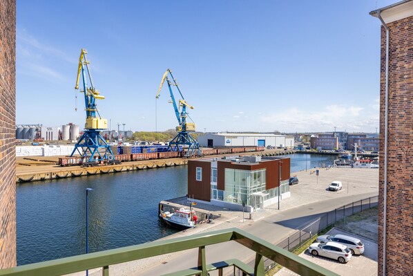 A waterfront industrial area with cranes, a dock, and a modern building with large windows.