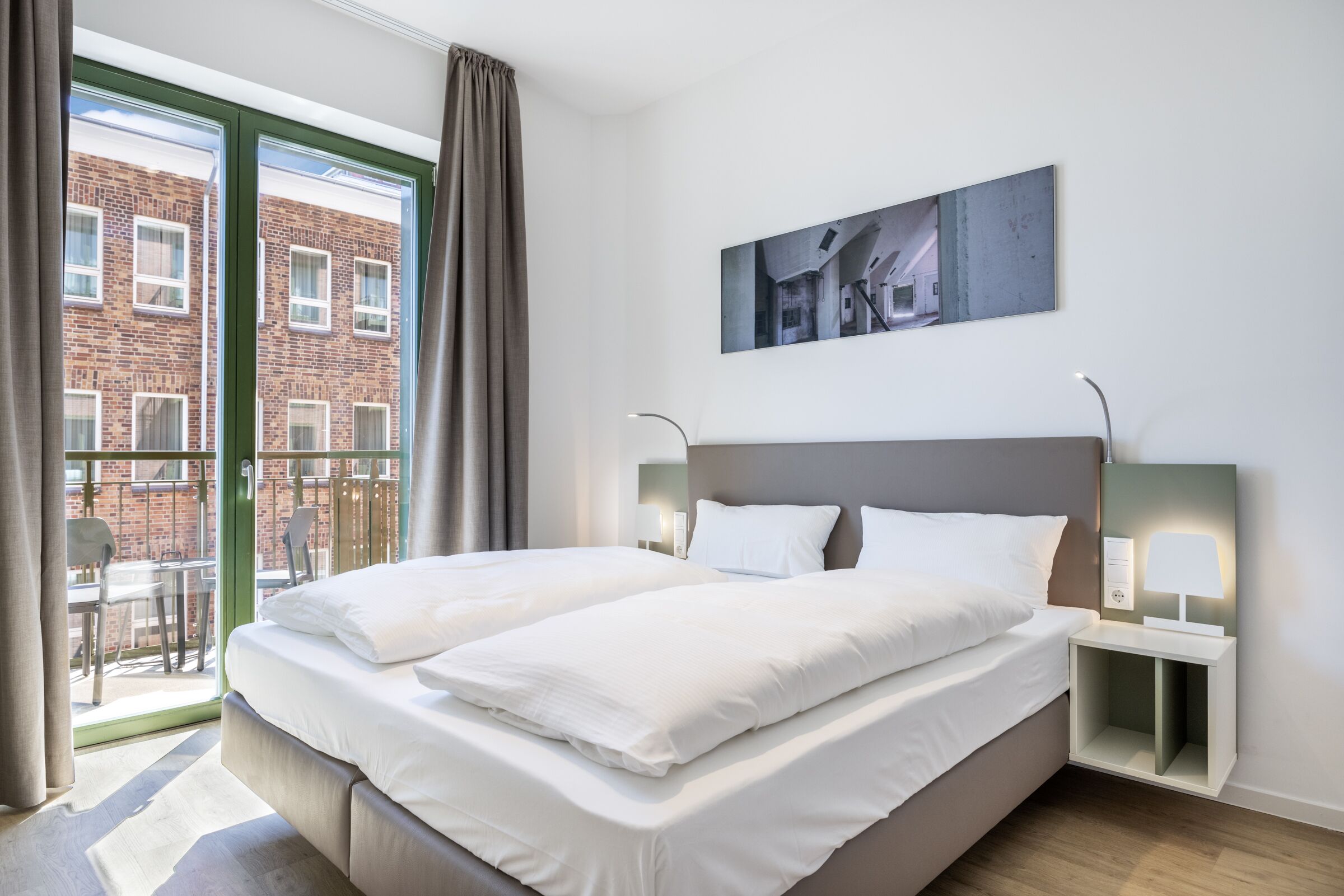 Quarto de hotel moderno com uma cama grande, uma varanda com vista para um edifício de tijolos e um quadro na parede.