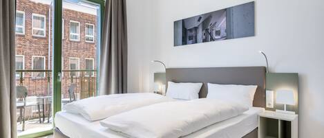 Quarto de hotel moderno com uma cama grande, uma varanda com vista para um edifício de tijolos e um quadro na parede.