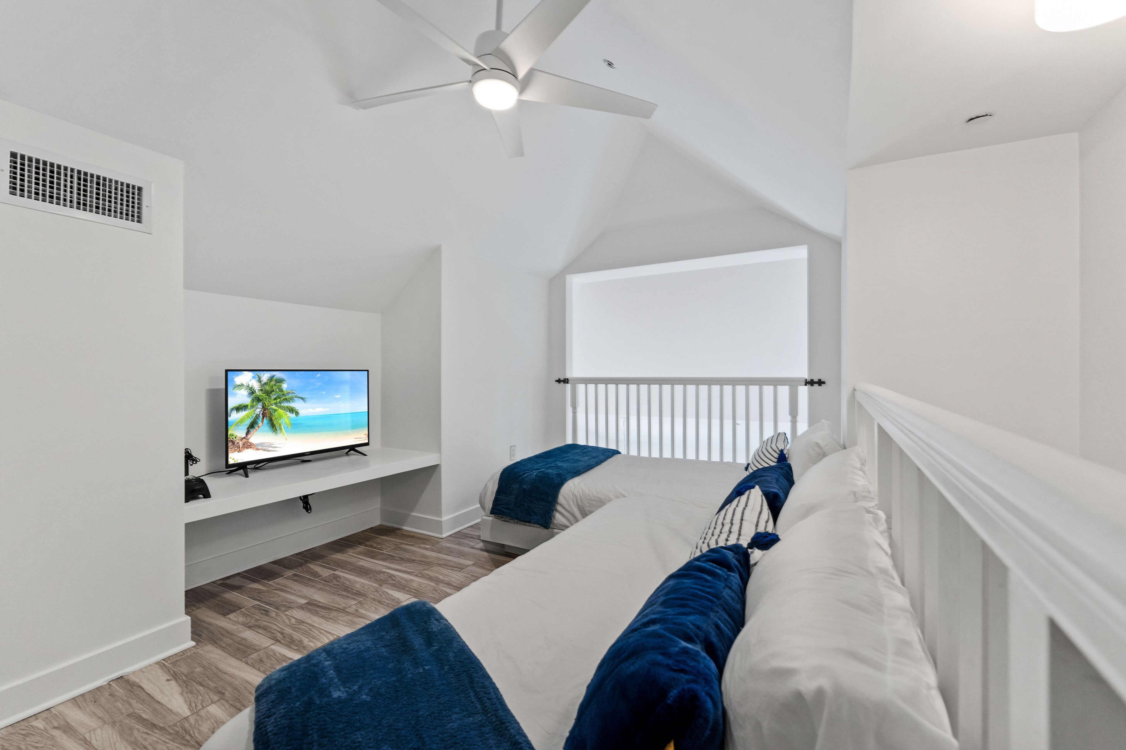 A bedroom with a bed, a TV on a stand, a ceiling fan, and a window.