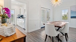 Un comedor con una mesa de madera y sillas blancas tapizadas, un centro de mesa decorativo y una lámpara de araña original.