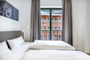 Una habitación de hotel moderna con una cama grande, vista a un edificio de ladrillo a través de la ventana y un cuadro en la pared.