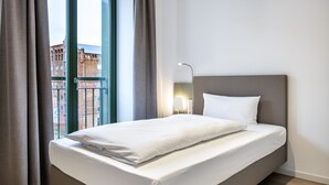 Ein ordentlich bezogenes Bett in einem Hotelzimmer mit Blick auf ein Gebäude durch ein Fenster.