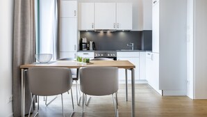A modern kitchen with white cabinets, a wooden table, two grey chairs, and stainless steel appliances. - Great south-facing harbor apartment with a direct view of Wismar's old harbor (Hansestadt Wismar)