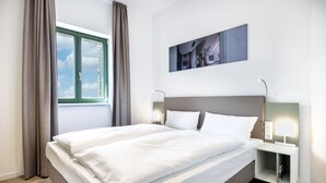 A modern hotel room with a large bed, a nightstand with a lamp, a window with curtains, and a wall-mounted picture. - Great south-facing harbor apartment with a direct view of Wismar's old harbor (Hansestadt Wismar)