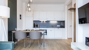 A modern kitchen with white cabinets, a dining area with two grey chairs, and a TV mounted on the wall. - Stilvolles, Modernes Hafenapartment mit Tollem Blick auf den Alten Hafen Wismars (Hansestadt Wismar)