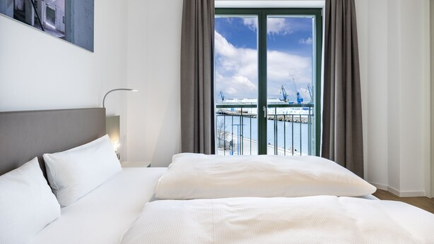 A hotel room with a large bed, a view of a marina through a sliding glass door, and a framed picture on the wall. - Stilvolles, Modernes Hafenapartment mit Tollem Blick auf den Alten Hafen Wismars (Hansestadt Wismar)