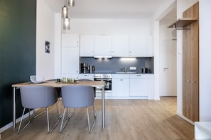 Une cuisine moderne avec des meubles blancs, une table à manger en bois et deux chaises grises.