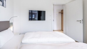 A modern hotel room with a large bed, a flat-screen TV mounted on the wall, and a walk-in closet.
