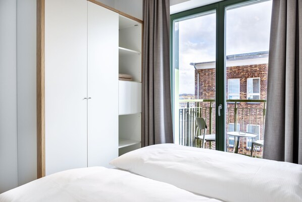 A bedroom with a bed, a wardrobe, and a balcony with a view of a brick building.