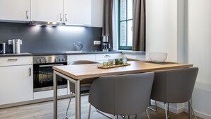 A modern kitchen with stainless steel appliances, a wooden table, and two grey chairs.