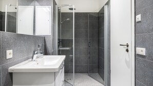 A modern bathroom with a white sink, a glass shower enclosure, and dark tiled walls. - Helles, Geschmackvolles Apartment in Erstklassiger Lage am Seehafen von Wismar (Hansestadt Wismar)