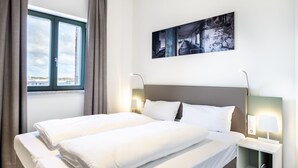 A hotel room with a large bed, two bedside tables with lamps, a window with curtains, and a wall-mounted painting. - Helles, Geschmackvolles Apartment in Erstklassiger Lage am Seehafen von Wismar (Hansestadt Wismar)