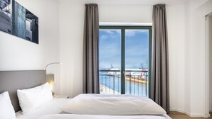 Una habitación de hotel con una cama grande, vista al agua y un cuadro en la pared.