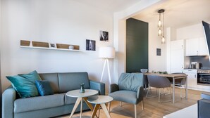 Una sala de estar moderna con un sofá gris, una mesita redonda y un comedor con una mesa y sillas blancas.