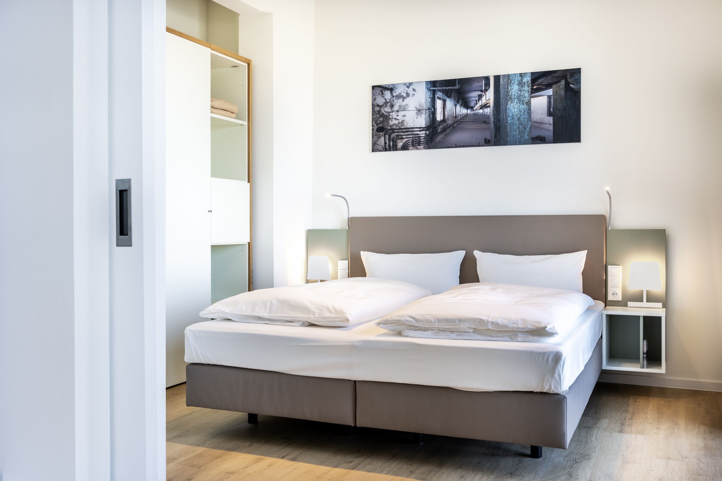 Une chambre moderne avec un grand lit, des tables de chevet et une œuvre d’art accrochée au mur.